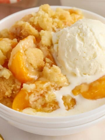 Peach cobbler in a white bowl topped with ice cream.