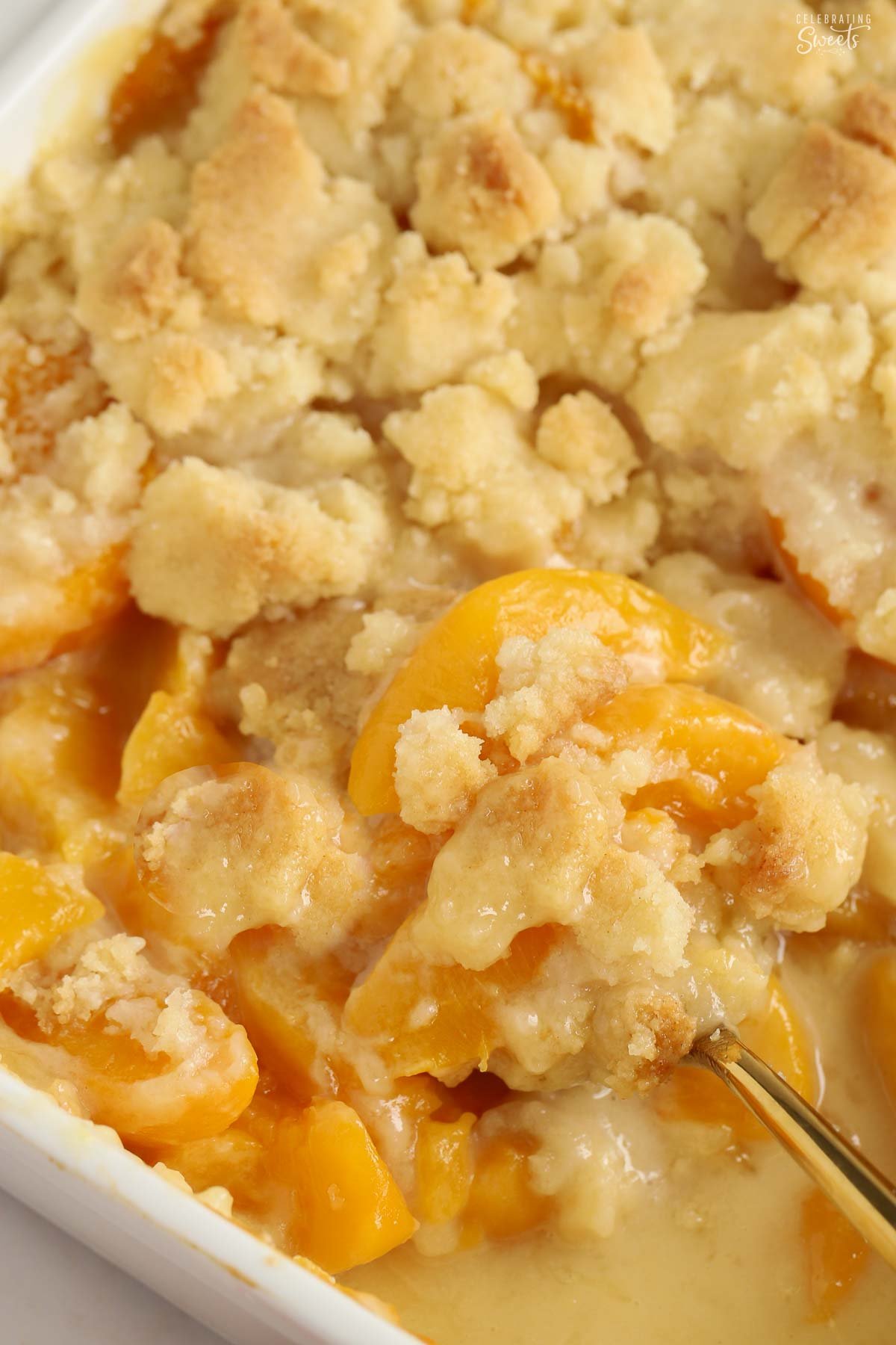 Peach cobbler in a baking dish with a gold spoon.