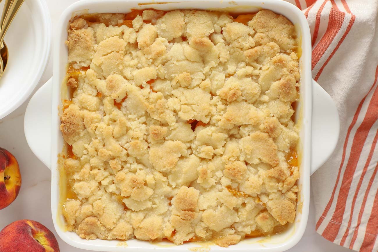 Peach cobbler in a white square baking dish next to an orange and white striped napkin.