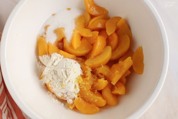 Peaches, flour, sugar, and lemon zest in a white bowl.
