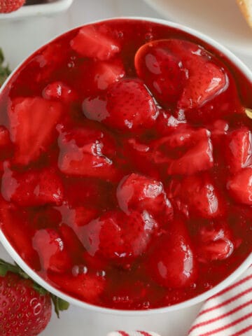 Strawberry sauce in a white bowl with a gold spoon