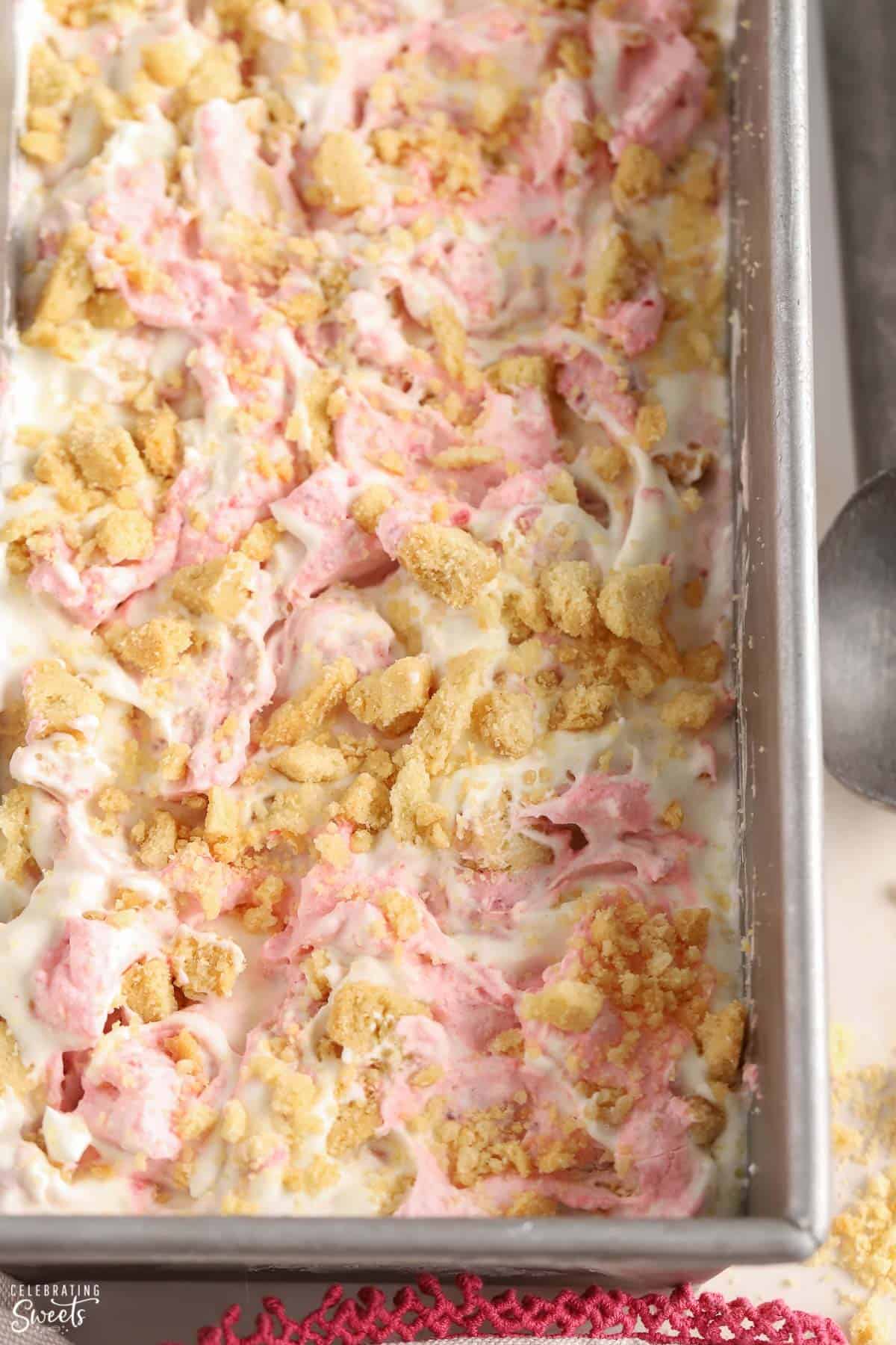 Strawberry shortcake ice cream in a loaf pan topped with crumbled shortbread cookies