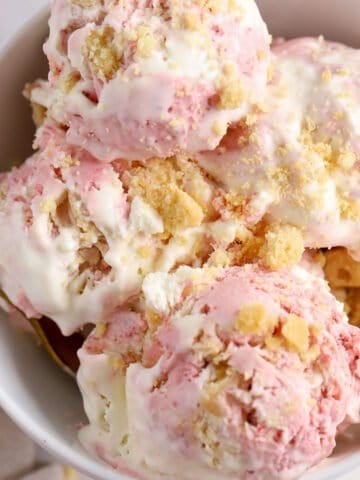 Scoops of strawberry shortcake ice cream in a white bowl.