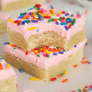 Two sugar cookie bars topped with pink frosting and sprinkles stacked on top of each other.