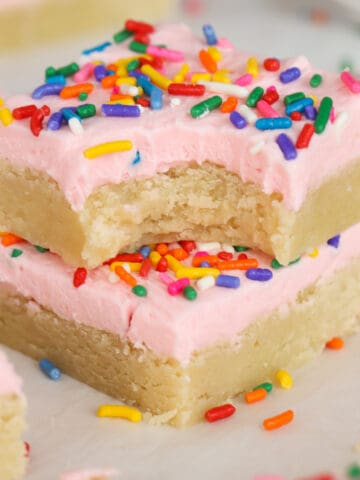 Two sugar cookie bars topped with pink frosting and sprinkles stacked on top of each other.