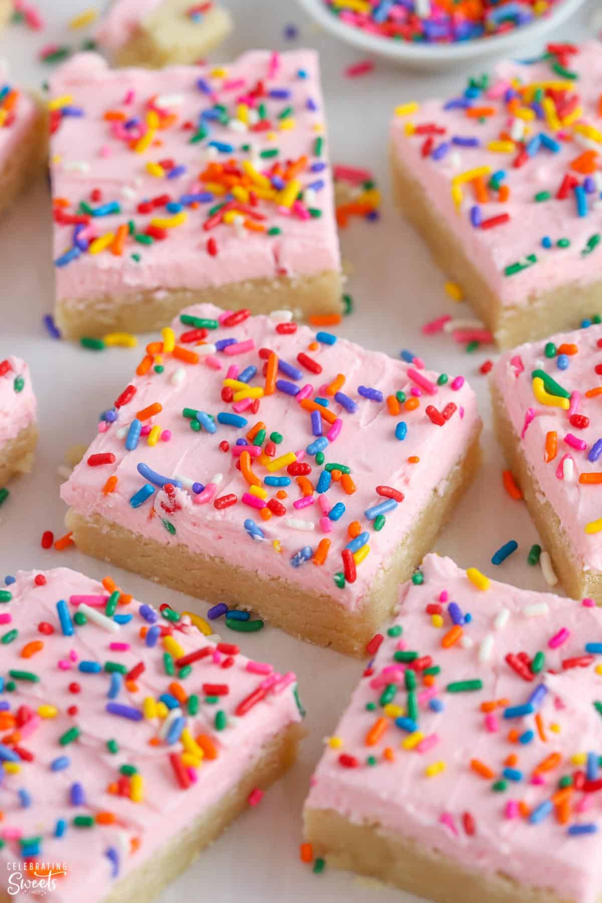 Sugar cookie bars topped with pink frosting and sprinkles.