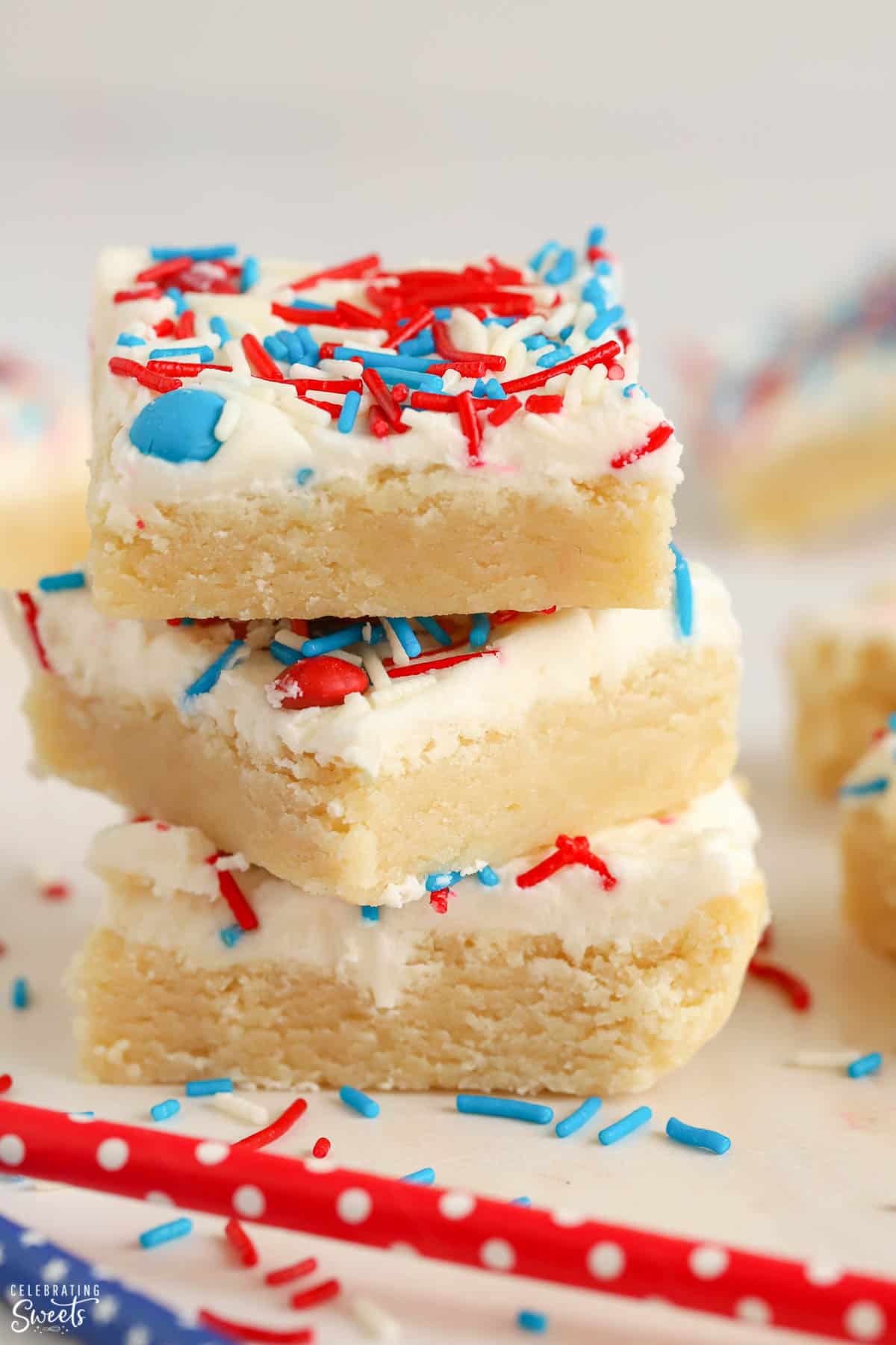 Stack of three sugar cookie bars topped with white frosting and red and blue sprinkles.