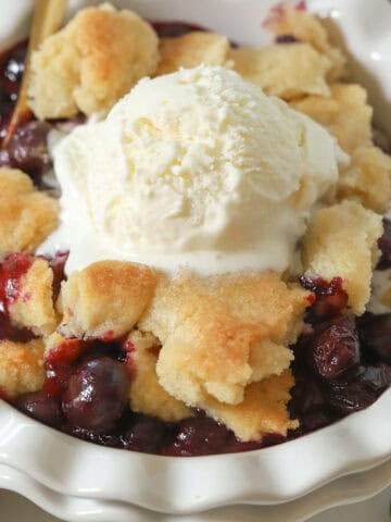 Blueberry cobbler in a white bowl topped with vanilla ice cream.