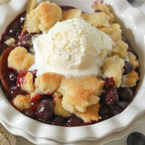 Blueberry cobbler in a white bowl topped with vanilla ice cream.