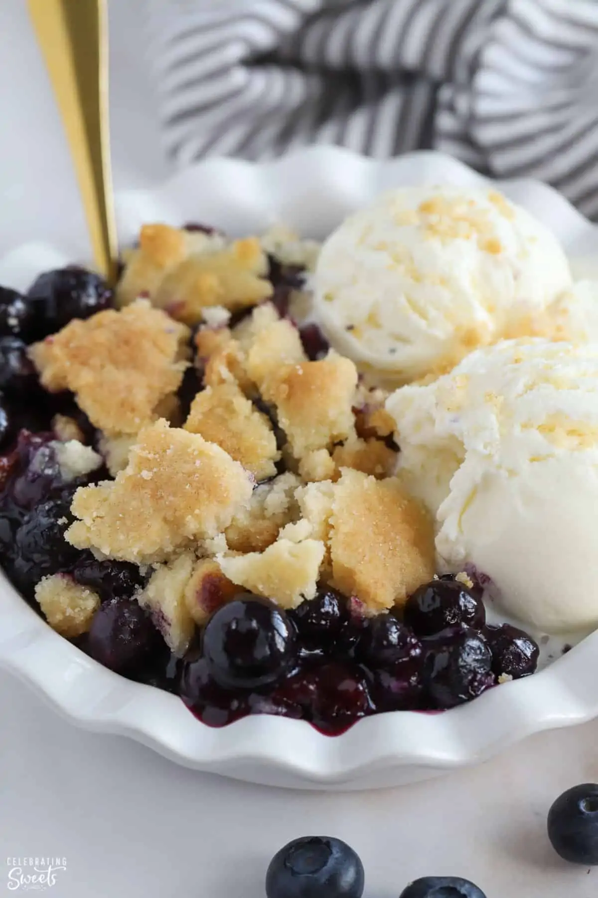 Closeup of blueberry cobbler in a white bowl topped with ice cream.