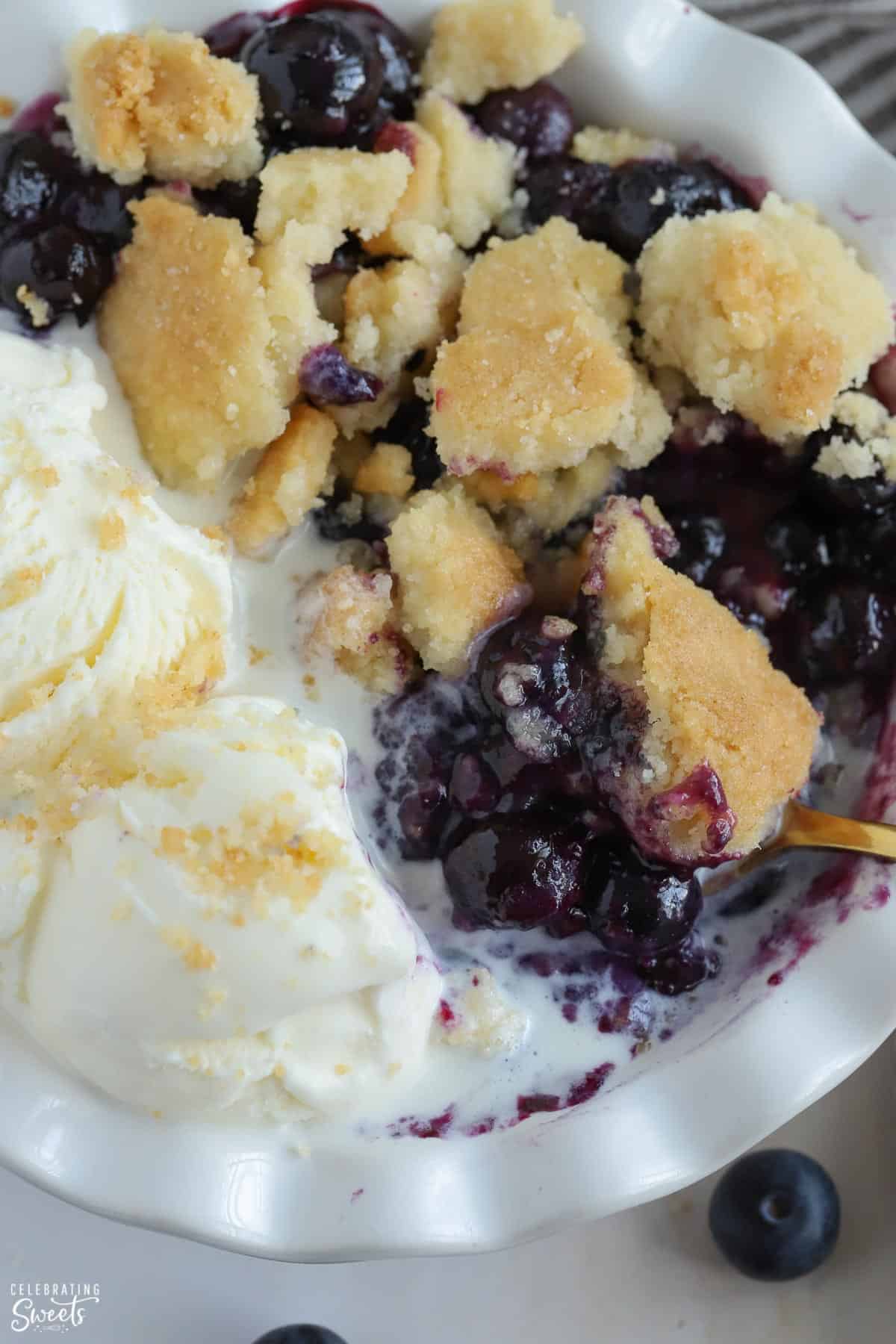 Closeup of blueberry cobbler in a white bowl topped with ice cream.