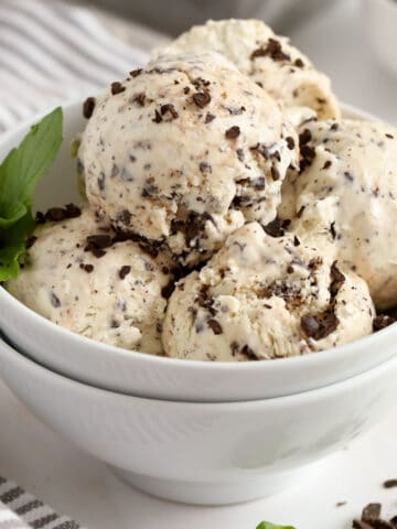 Scoops of mint chip ice cream in a white bowl garnished with fresh mint.