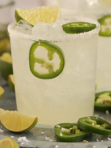 Spicy Margarita in a glass on a tray garnished with lime and jalapeno slices.