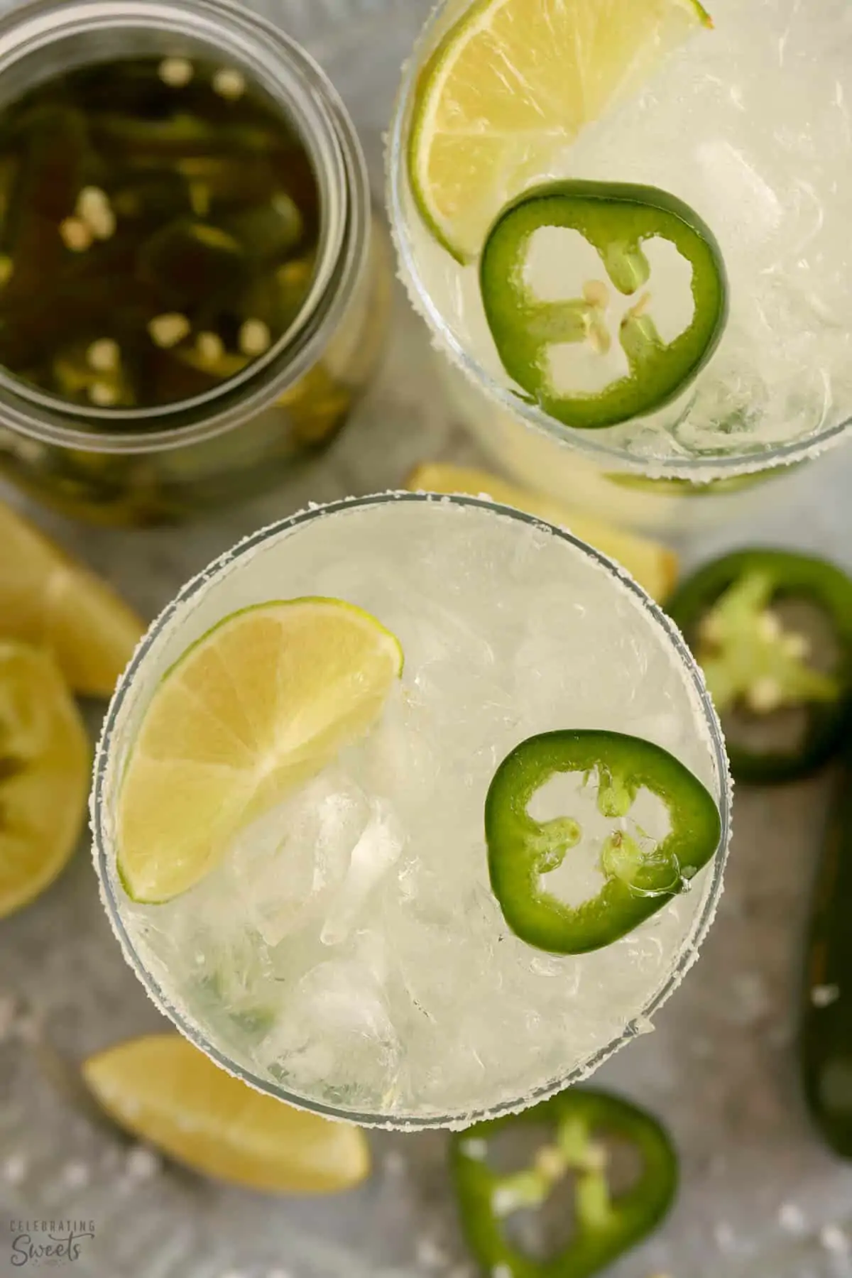 Overhead shot of two spicy margaritas garnished with lime and jalapeno.