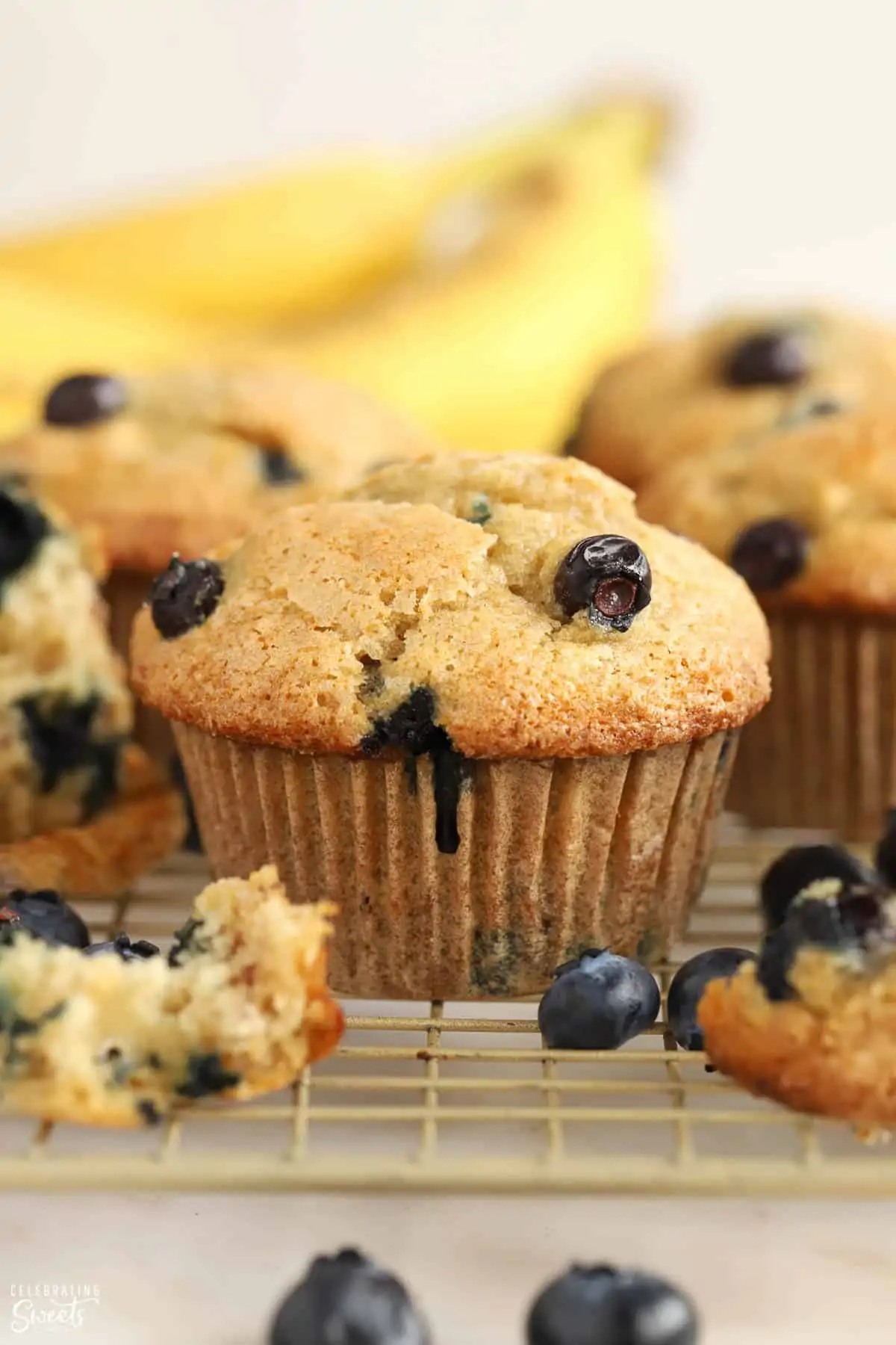 Closeup of blueberry banana muffins on a wire rack with bananas in the background.
