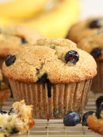 Closeup of blueberry banana muffins on a wire rack with bananas in the background.