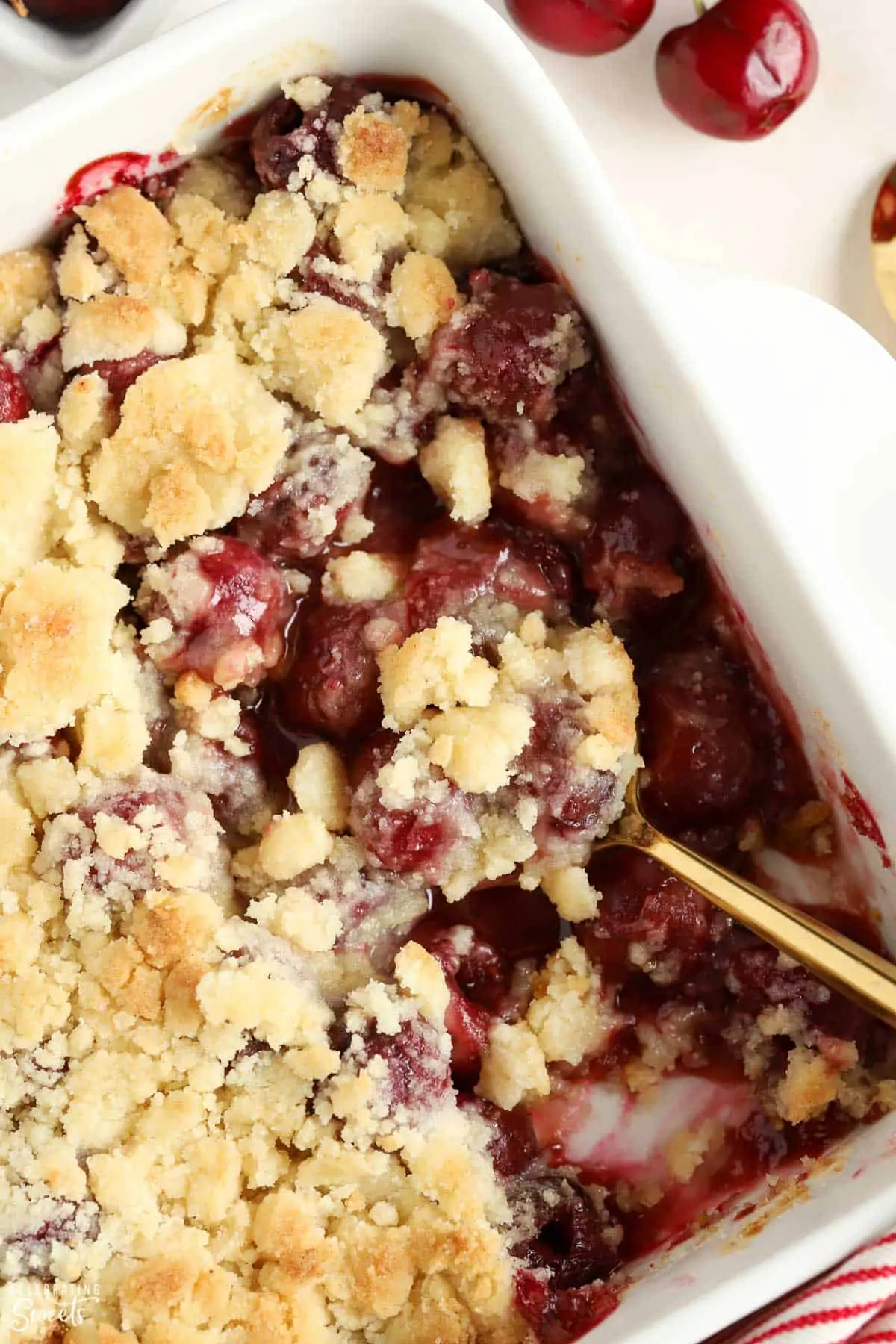 Cherry cobbler in a white baking dish with a gold spoon.