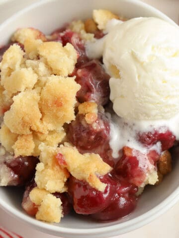 Cherry cobbler in a white bowl topped with vanilla ice cream.