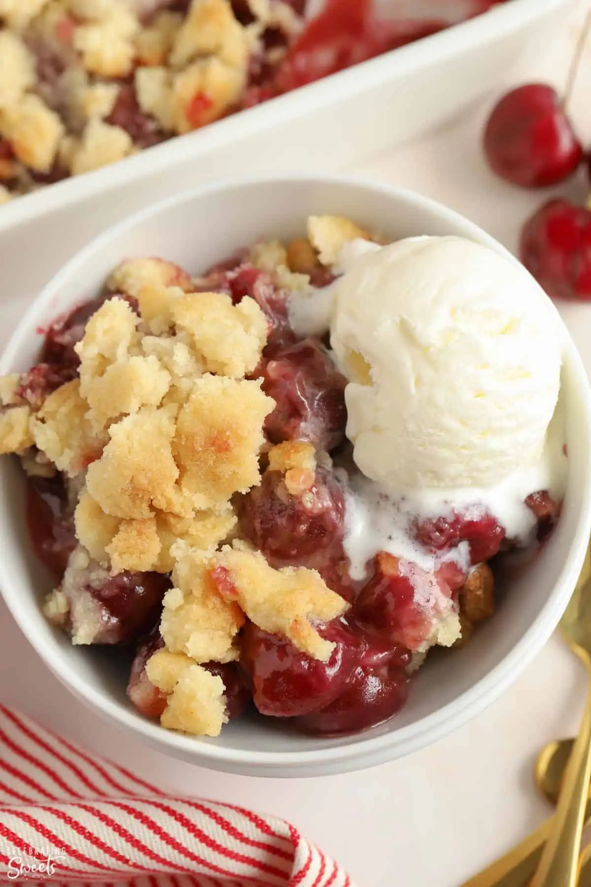 Cherry cobbler in a white bowl topped with vanilla ice cream.