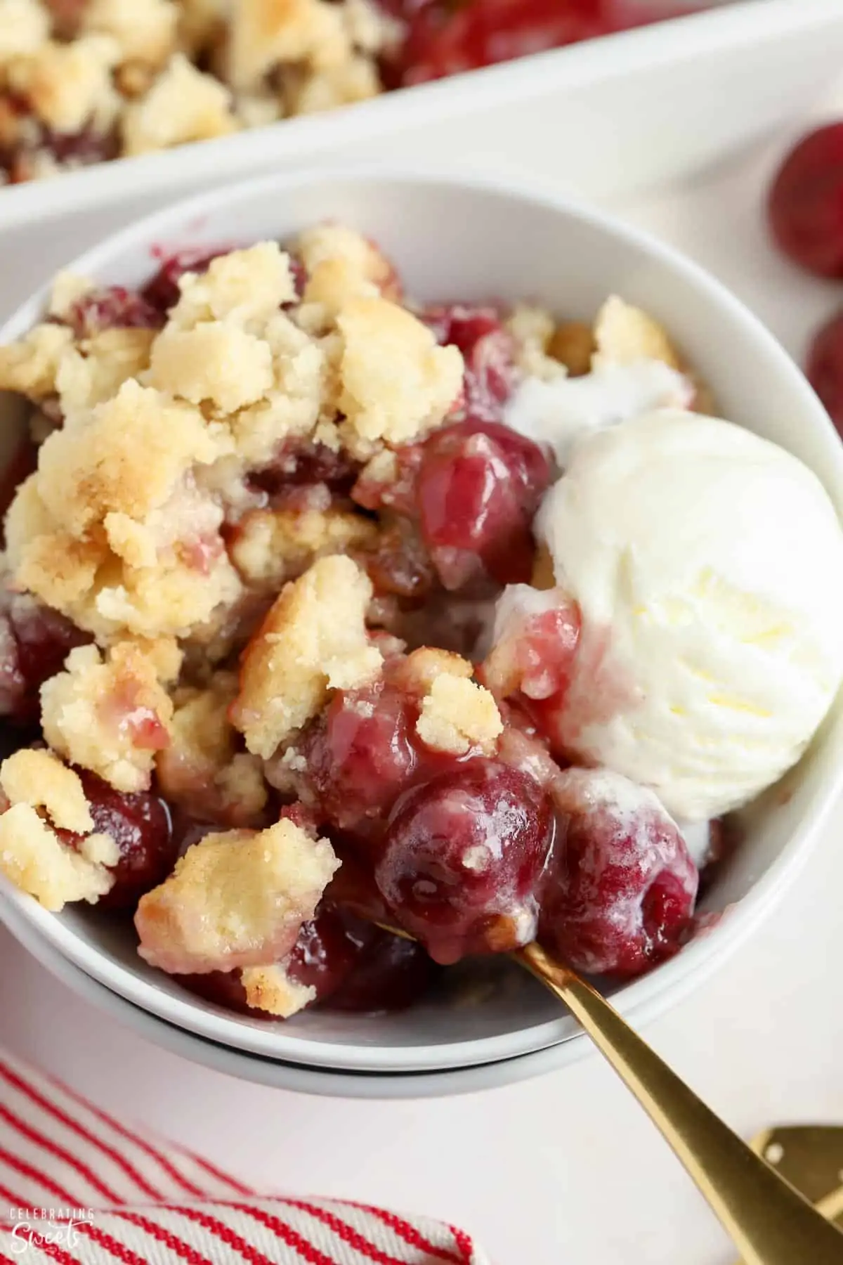 Cherry cobbler in a white bowl topped with vanilla ice cream.