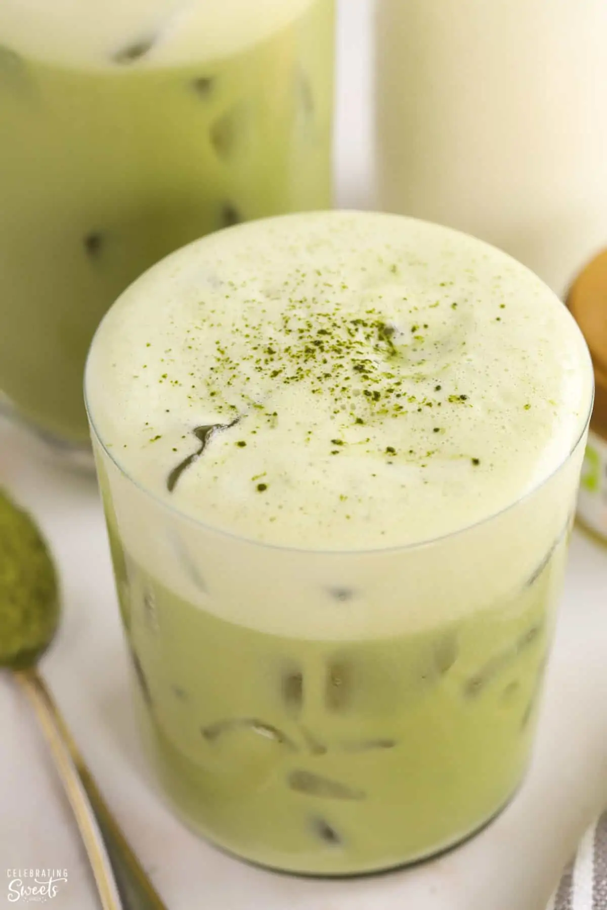 Closeup of an iced matcha latte in a glass toped with a sprinkling of matcha powder
