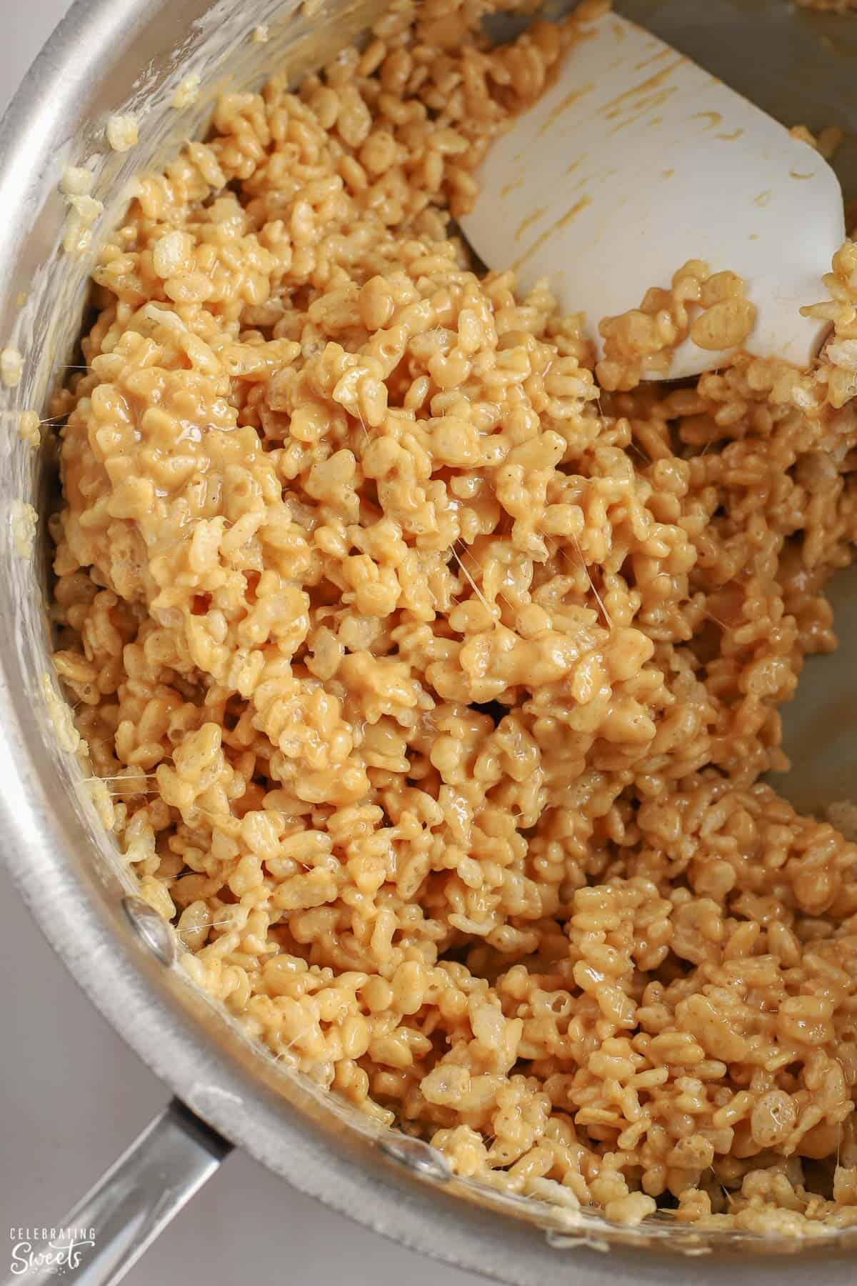 Peanut butter rice krispies in a large saucepan with a white spatula.