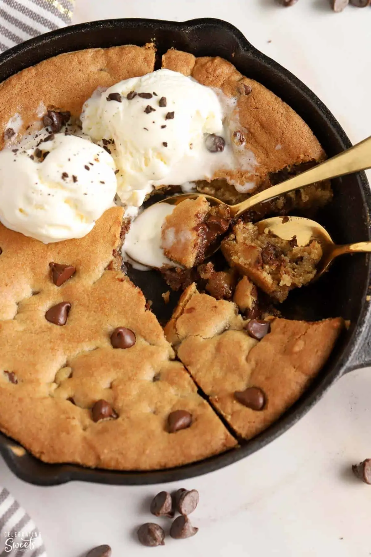 Chocolate chip skillet cookie in a cast iron skillet with vanilla ice cream and two gold spoons.