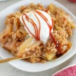 Apple crisp on a white plate topped with vanilla ice cream and caramel sauce.