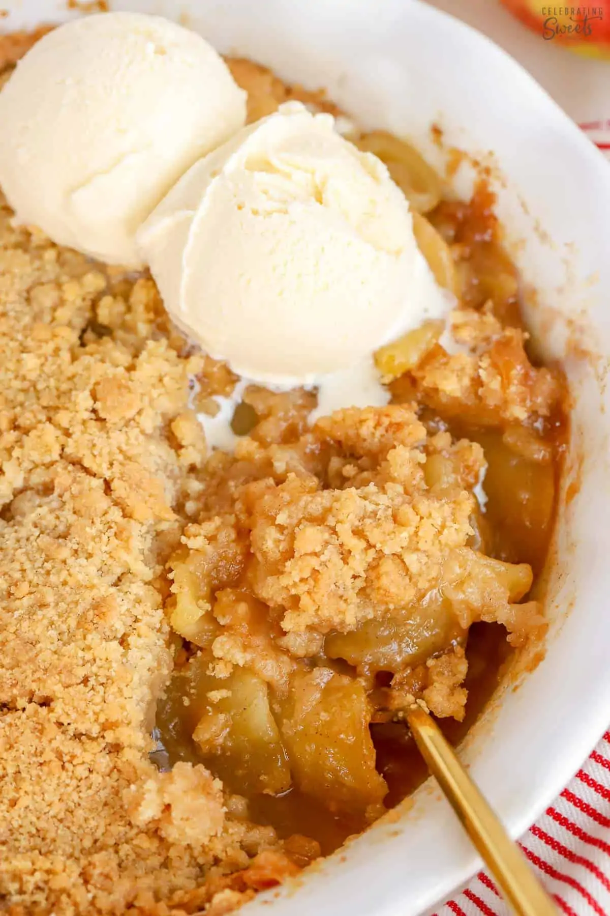 Apple crumble topped with two scoops of vanilla ice cream in a white baking dish.
