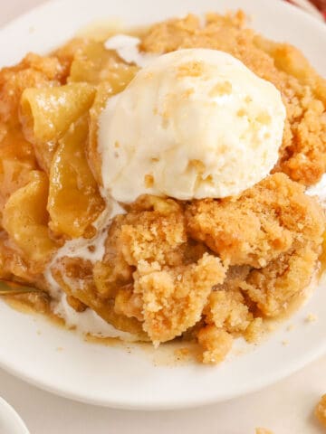 Apple crumble on a white plate topped with a scoop of melty vanilla ice cream.