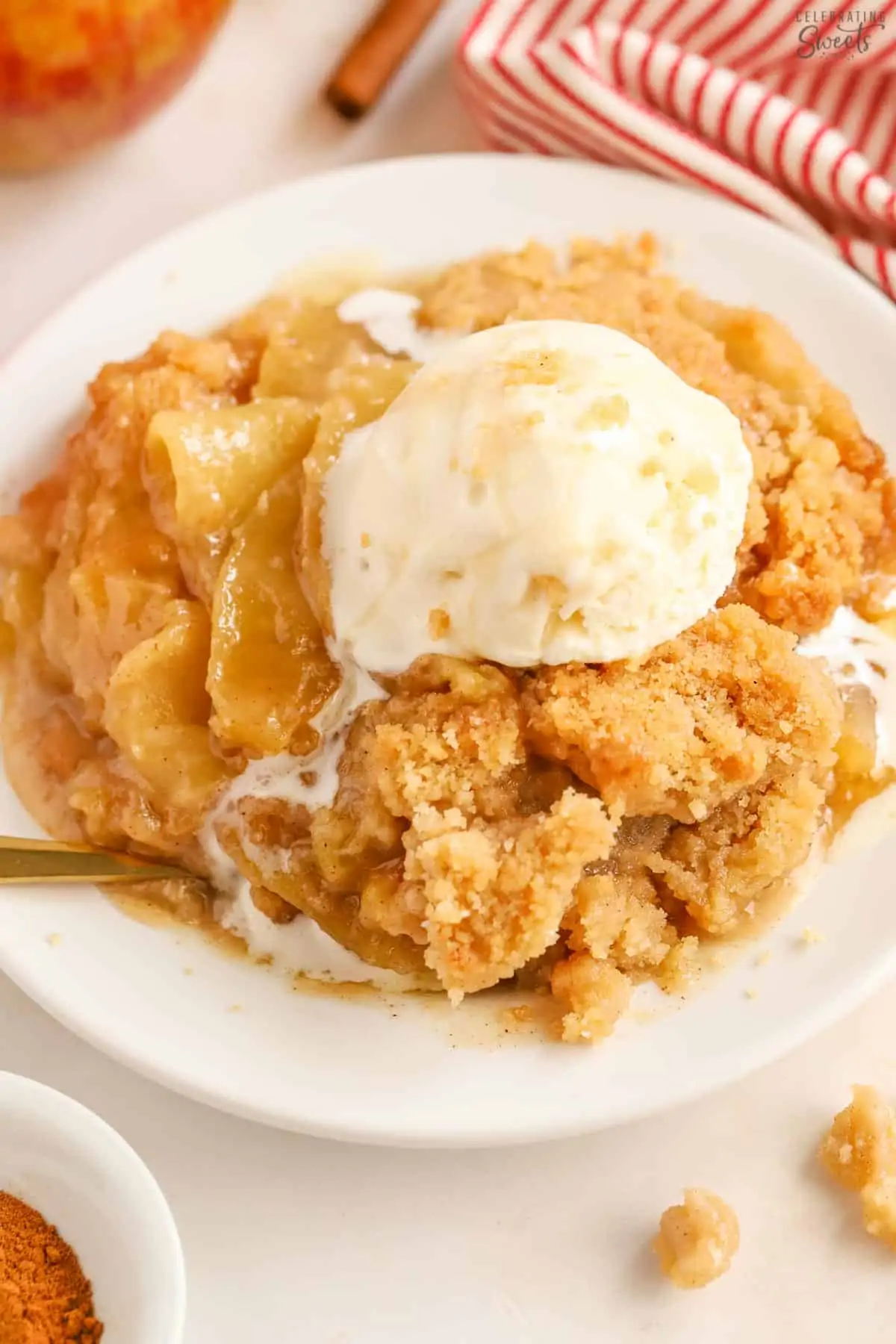 Apple crumble on a white plate topped with a scoop of melty vanilla ice cream.