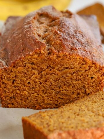 Loaf of pumpkin banana bread on a white board with bananas in the background.