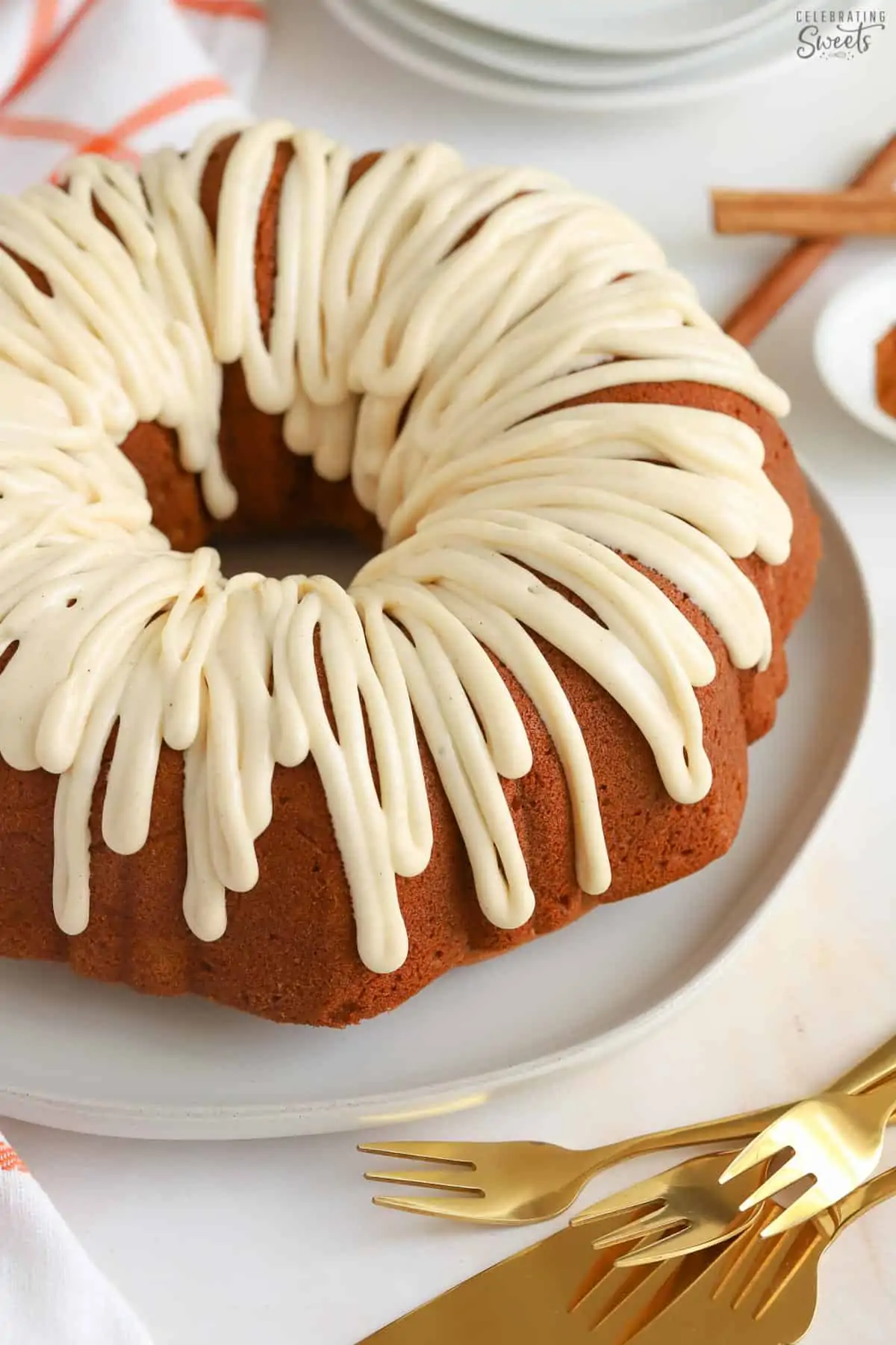 Pumpkin bundt cake drizzled with white icing sitting on a white plate next to gold forks.