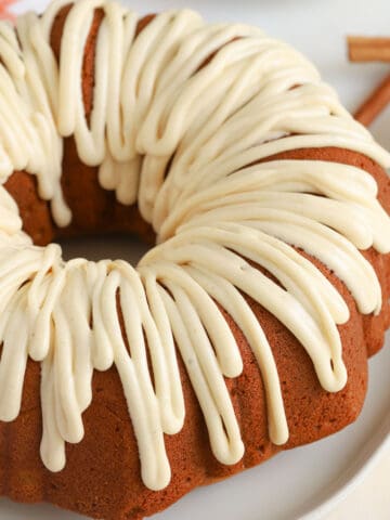 Pumpkin bundt cake drizzled with white icing sitting on a white plate.