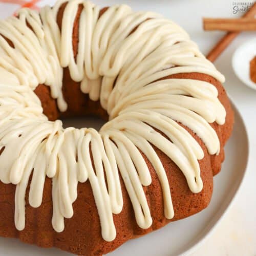 Pumpkin bundt cake drizzled with white icing sitting on a white plate.