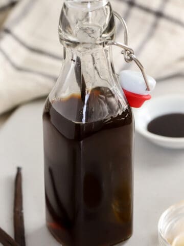 Vanilla extract in a glass container with vanilla beans next to it.