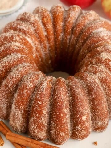 Apple Cider Donut Cake covered in cinnamon sugar on a round white plate.