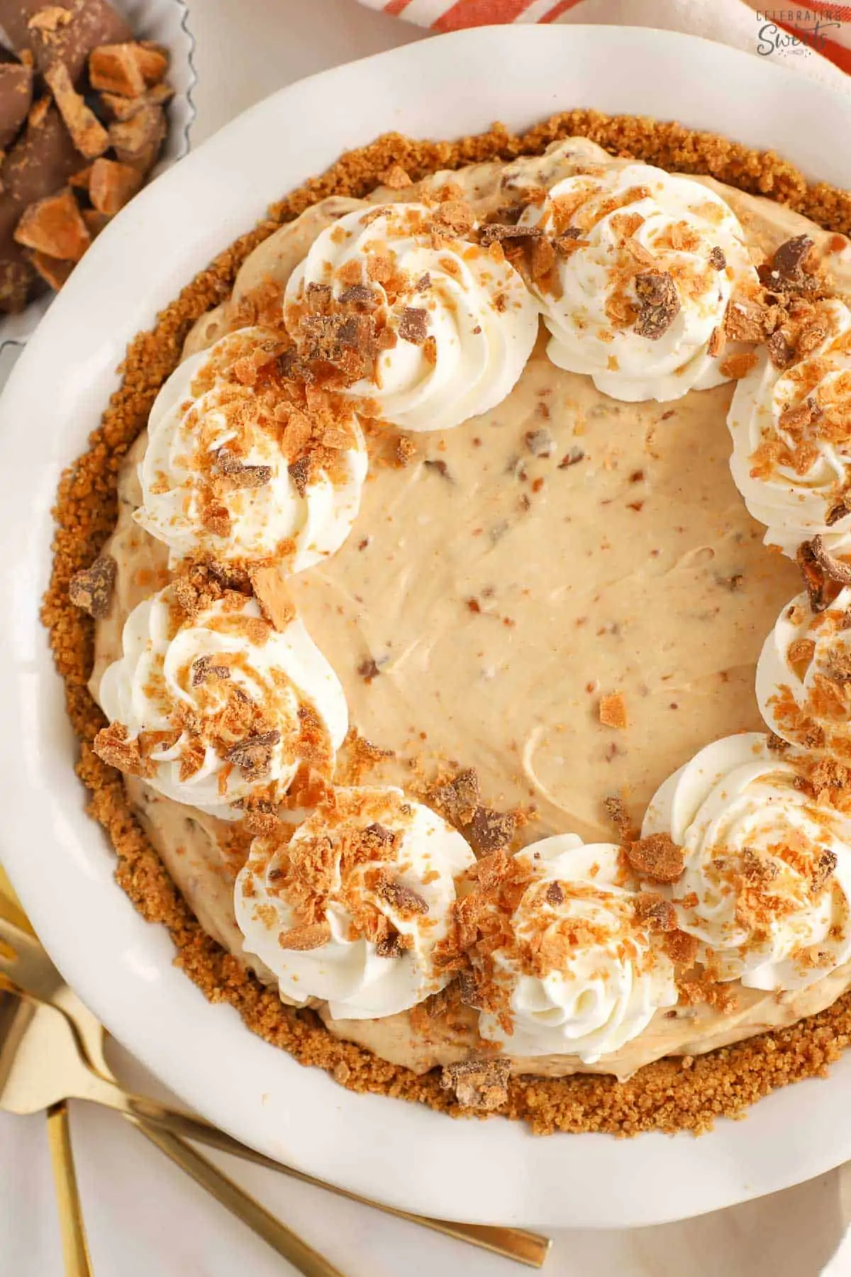 Butterfinger pie in a white pie plate topped with swirls of whipped cream.
