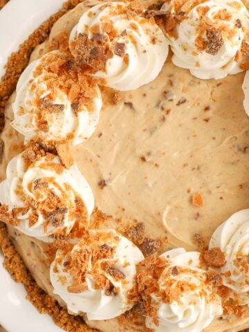 Butterfinger pie in a white pie plate topped with swirls of whipped cream.