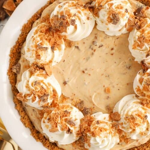 Butterfinger pie in a white pie plate topped with swirls of whipped cream.