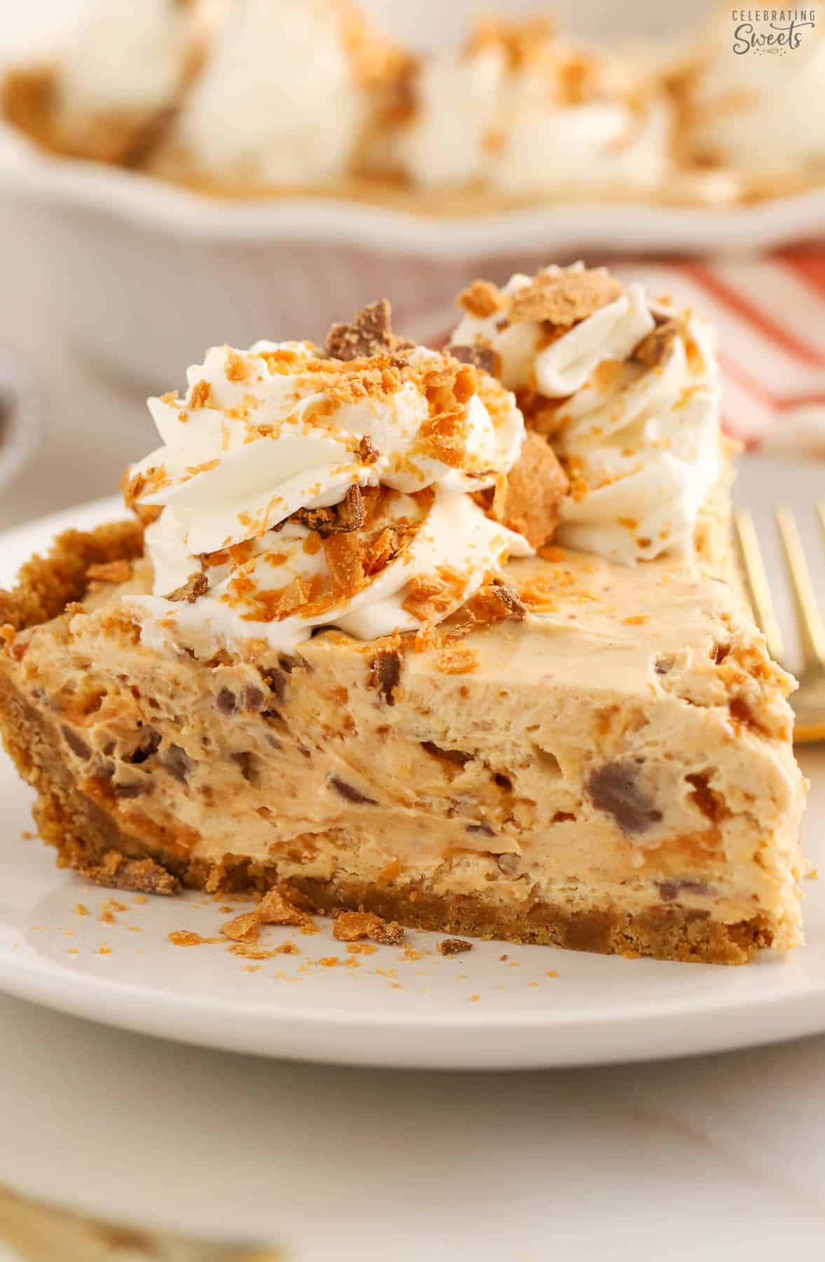 Slice of Butterfinger pie on a white plate garnished with whipped cream and crushed Butterfinger.