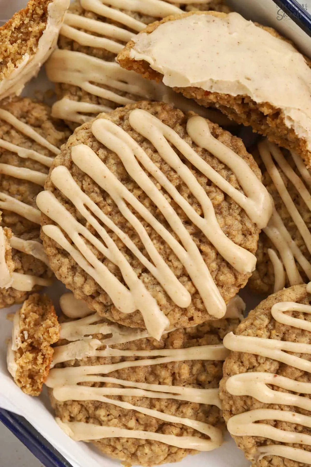 Pile of oatmeal cookies topped with maple icing on a blue and white tray.
