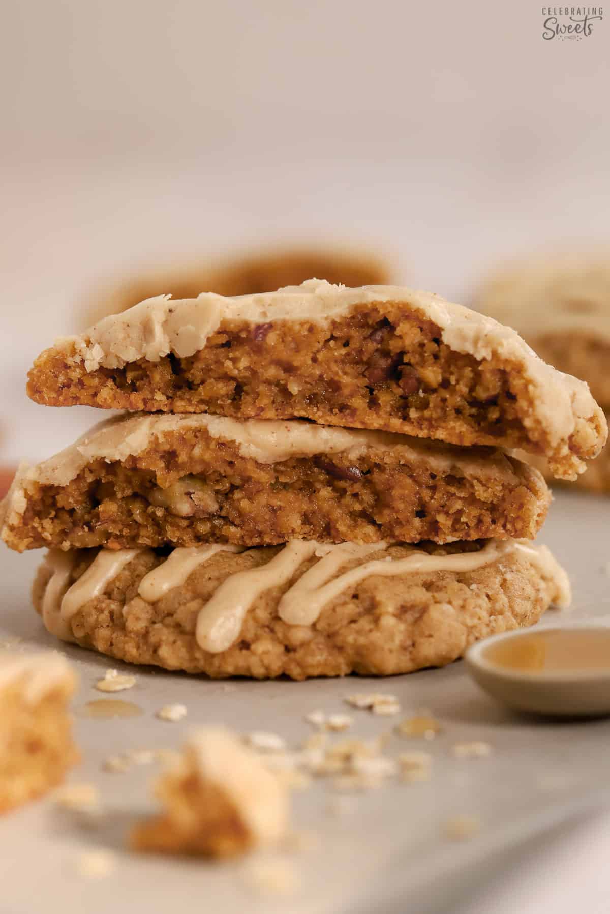 Stack of maple oatmeal cookies surrounded by oats and a spoon filled with syrup.