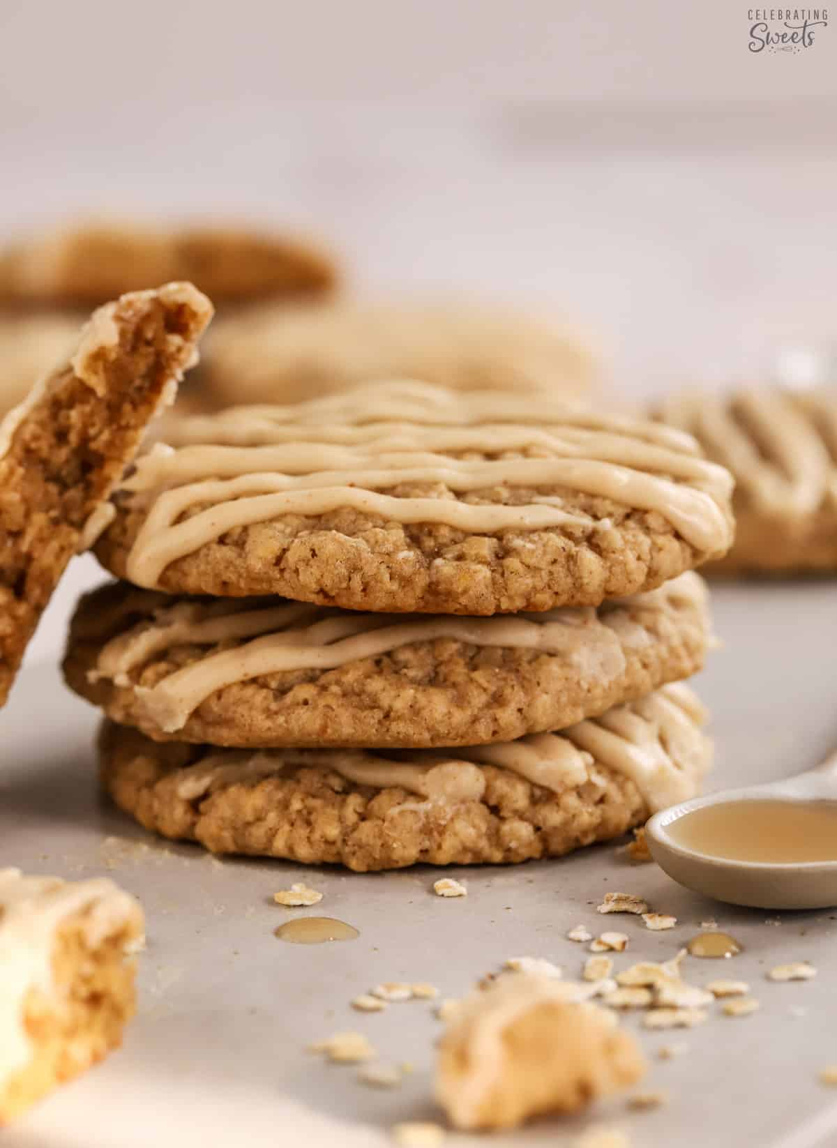 Stack of maple oatmeal cookies surrounded by oats and a spoon filled with syrup.