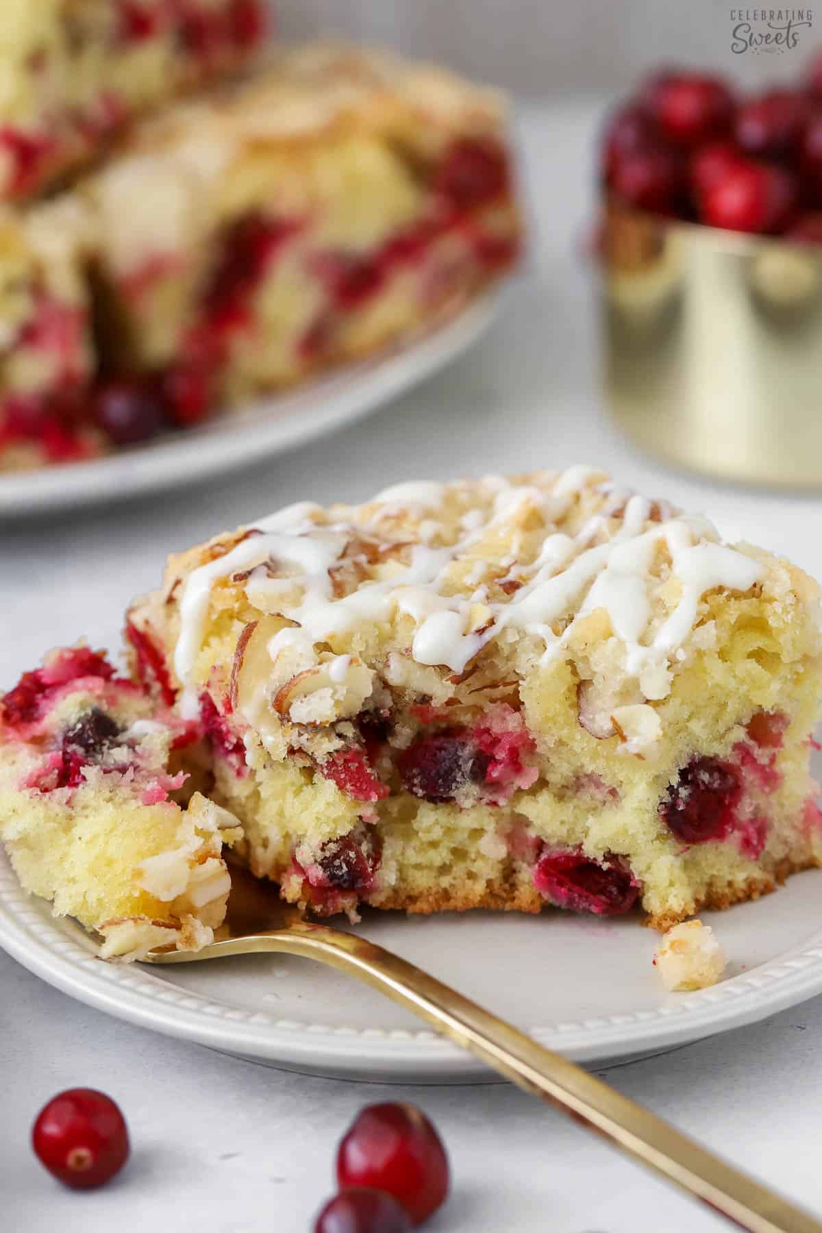 Slice of cranberry cake on a plate with a gold fork.