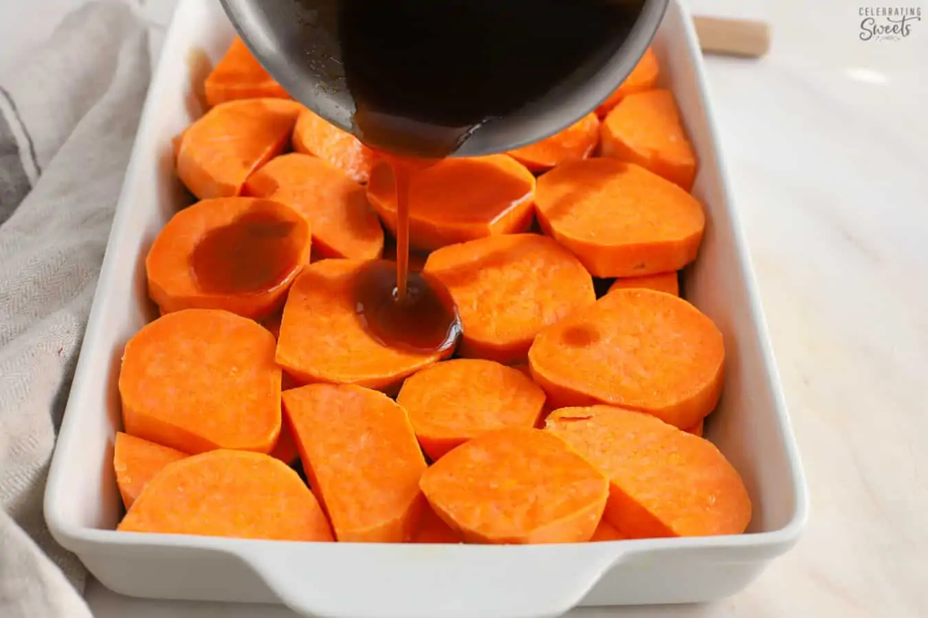 Brown sauce being poured over chopped sweet potatoes in a white baking dish.