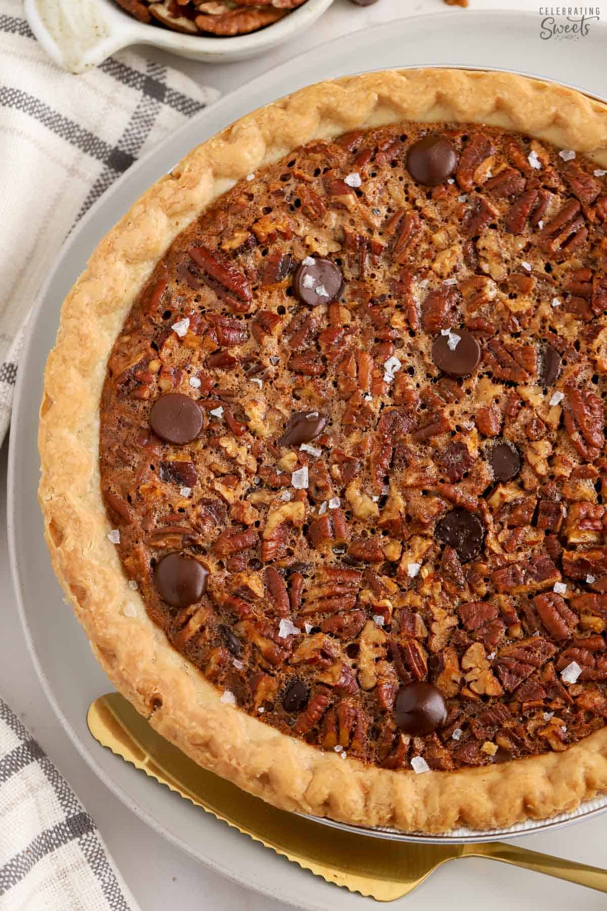 Overhead shot of chocolate pecan pie on a grey plate with a gold pie server.