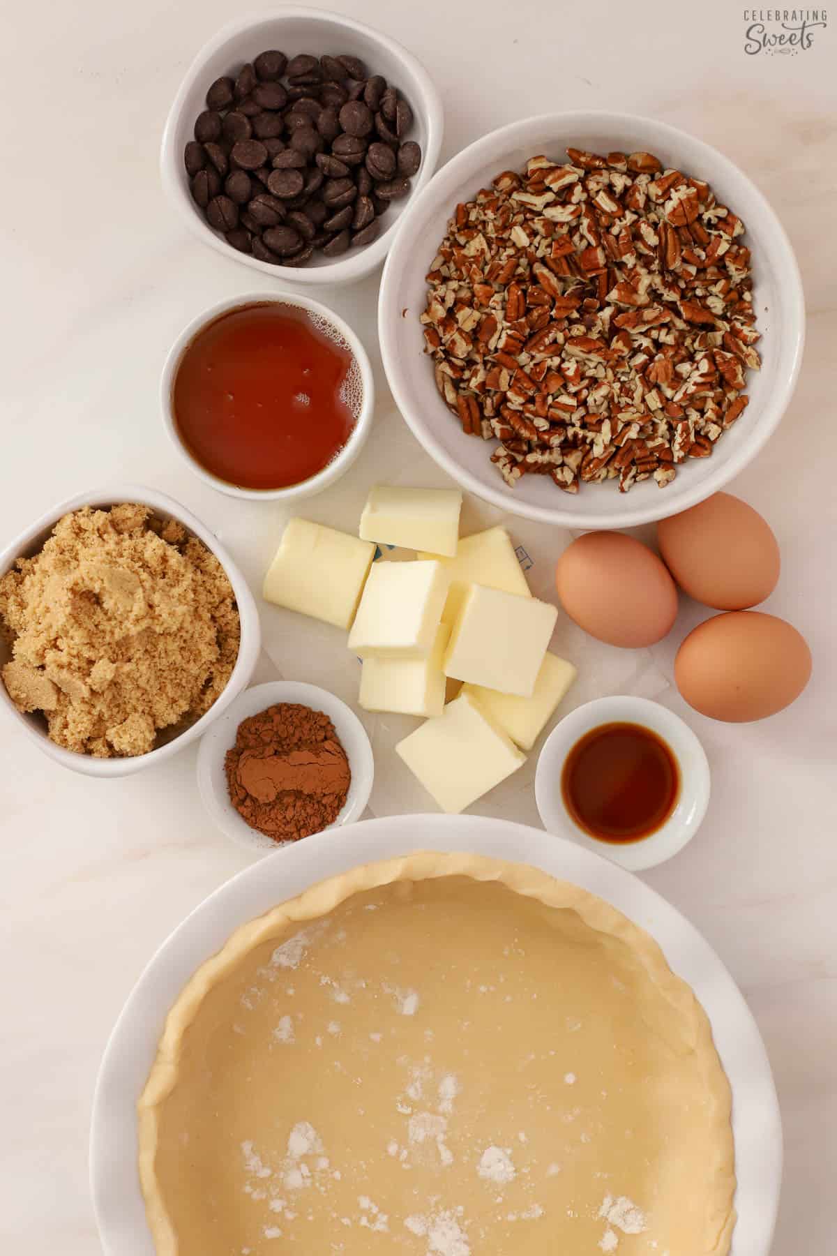 Ingredients for chocolate pecan pie - pie crust, syrup, sugar, chocolate chips, cocoa powder, pecans, vanilla, butter, eggs.