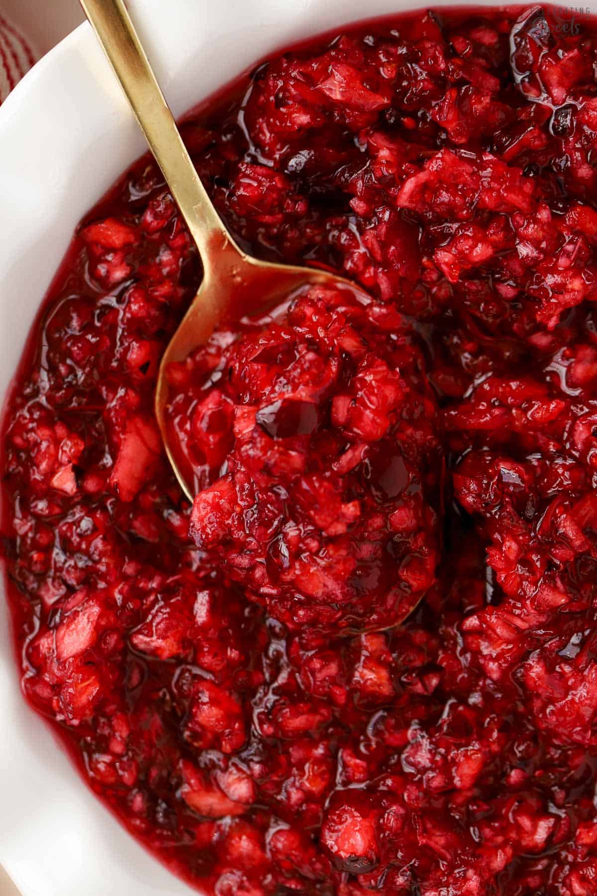 Closeup of cranberry orange relish in a white bowl with a gold spoon.