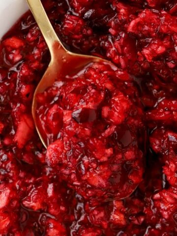 Closeup of cranberry orange relish in a white bowl with a gold spoon.